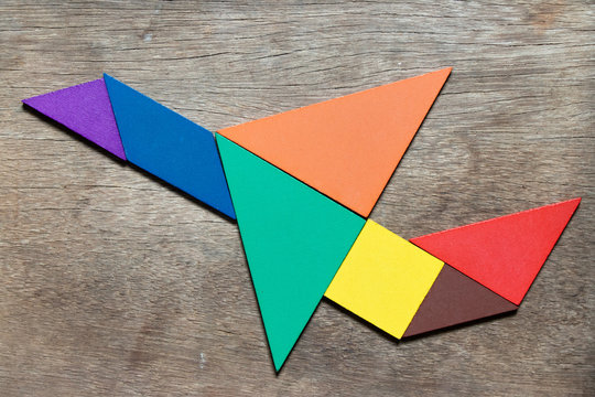 Color tangram puzzle in flying airplane shape on wood background