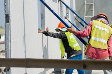 Construction worker are installing the precast concrete wall, orange safety helmet and green vest.