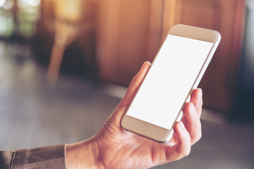 Mockup image of hand holding and using a white mobile phone with blank screen with blurred background in cafe