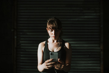 Sporty woman listening to music in a dark alley