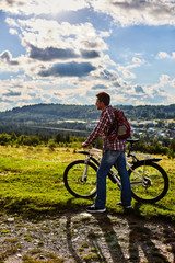 Fototapeta na wymiar A man in nature with a bicycle on the background of mountains and blue sky