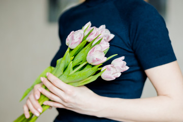 woman holding a beautiful colourful blossoming flower bouquet of fresh white pink tulips, ranunculus,leaves on the grey wall background.bouquet of spring flowers in her hands. Mothers day concept