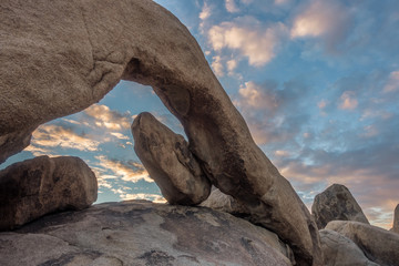 Natural rock arch and glowing puffy clouds at sunrise, Joshua Tree National Park, California