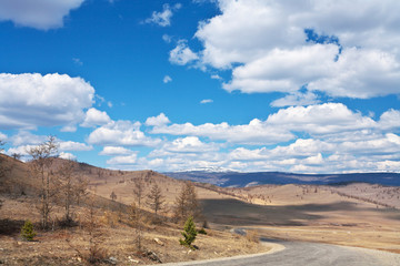 Fototapeta na wymiar The road along the Tazheranskaya steppe to Lake Baikal. Spring landscape on the background of a beautiful sky with cumulus clouds