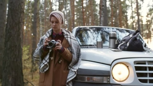 Medium shot of young woman in beanie taking photo with camera during forest trip in autumn