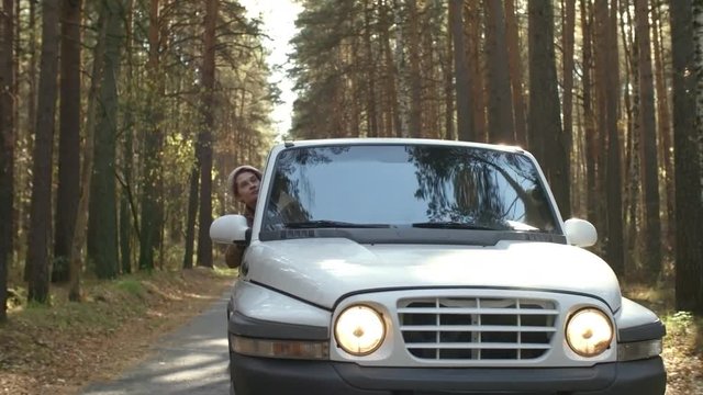 Front view of silver crossover moving towards camera on forest road, woman looking out of window and enjoying nature