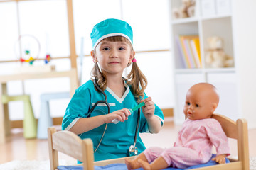 An active preschool child little girl dressed as doctor plays with her doll in nursery