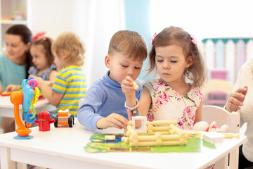 Group of kids play in kindergarten. Children building toy house with plastic blocks sitting together by the table