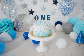 Photo zone with paper stars, balloons, paper honeycombs, paper balls, pom poms, confetti and cream cake. Birthday cake. Smash cake. One year. Blue, white, grey, turquoise colors.