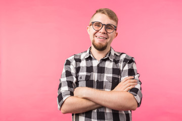 Portrait of happy fashionable handsome man in plaid shirt and glasses crossing hands on pink background