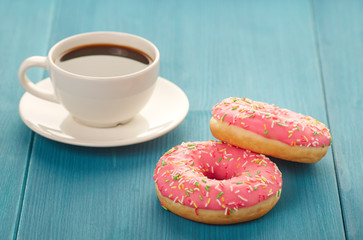 Naklejka na ściany i meble Pink donuts with a cup of coffee on a wooden table. Sweet donuts