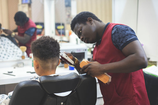 Cute african american boy in the african barbershop. Cute mixed boy makes a haircut in the African salon. Hair style. Haircut by machine for children. School boy hair style. Haircut by scissors. 