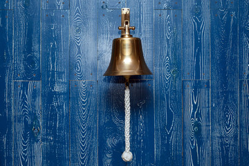 Copper old vintage bell, doorbell, rope on a wooden blue aged wall. Concept decor element in interior of deck, cabin of ship, restaurant, room, house decorated on marine theme