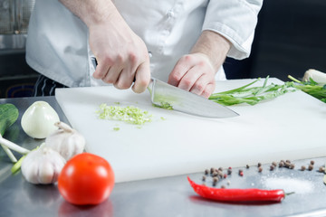 Closeup chef's hands cooking green onion for preparing healthy vegetable salad on acutting board in restaurant kitchen. Concept new lean menu, low calories speciality