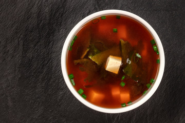 Miso shiru soup with tofu, scallions, and wakame seaweed, shot from the top on a black background with copy space