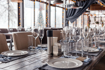 Restaurant serving, glass wine and water glasses, plates, spice set, forks and knives on textile napkins stand in a row on gray wooden table. Concept banquet, birthday, conference, group lunch