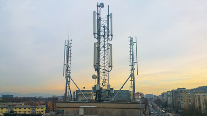 Fototapeta na wymiar Cellular network antenna radiating and broadcasting strong power signal waves over the city on a building roof with telecommunication mast
