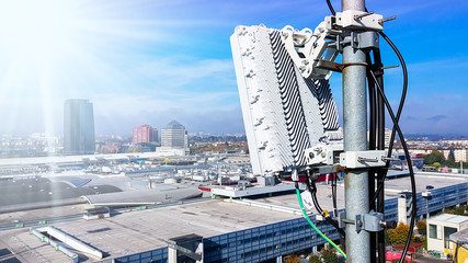 5G mobile telecommunication cellular radio network antenna on a mast on the roof broadcasting signal waves over the city on a clear sunny day with blue sky and clouds