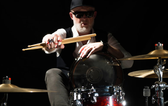 Drummer with a drumsticks in his hands sits behind drum kit on the black background