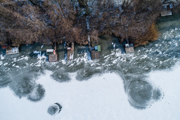 Aerial view of winter frozen lake with wooden houses on pier