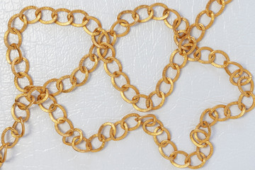 Gold color chain. Chain on white leather background.