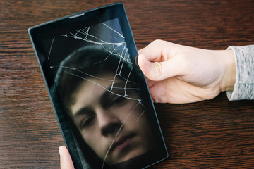 Reflection of the face of the teenager in the screen of the broken tablet. Teenage loneliness, depression.