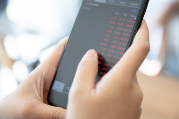 Female hand with smartphone trading stock online in coffee shop , Business concept