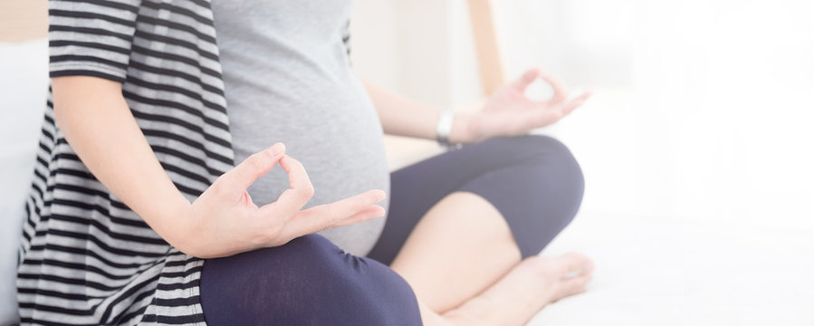 Torso close-up of pregnant woman working out indoors. Pregnant fitness woman sitting in yoga crossed-leg pose . Pregnancy Yoga concept.