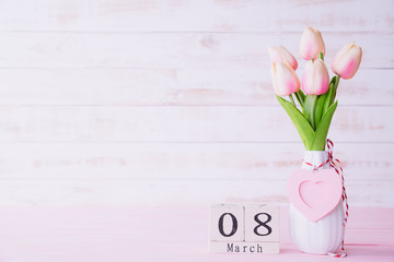 Womans day concept. Pink tulips and red heart with March 8 text on wooden block calendar on white wooden background.