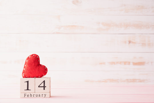 Valentines day concept. February 14 text on wooden block with handmade red heart on white wooden background.