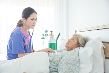 Senior female patient lying in bed while doctor exam by stethoscope at hospital ward