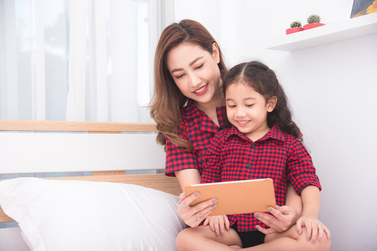 Beautiful asian mother and daughter using tablet computer together at home - Powered by Adobe