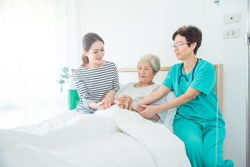 Doctor talking to elderly female patient lying in bed while patient's daughter sitting beside her...