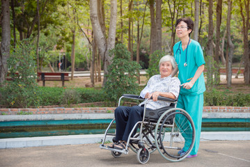 Happy asian senior woman on wheelchair with nurse in nursing home hospital garden