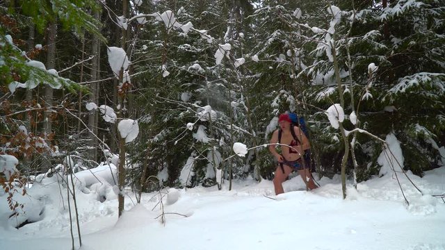 Undressed man with a backpack walking in the snow in the winter forest. The man is cold and trembling. Beautiful nature and trees covered with snow. 4K