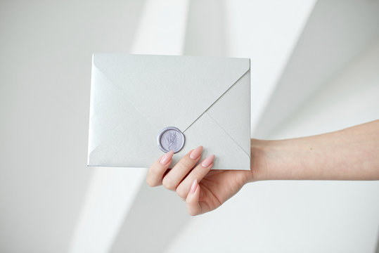 Close-up photo of female hands holding a silver invitation envelope with a wax seal, a gift certificate, a postcard, a wedding invitation card