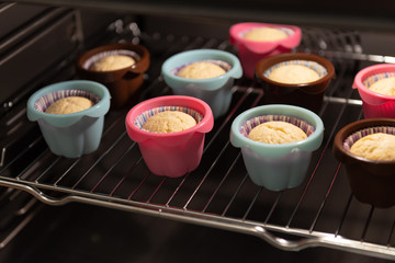 Muffins in ccolorful silicone molds growing up in the oven. Cupcakes, bakery. Close up