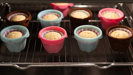 Muffins in ccolorful silicone molds growing up in the oven. Cupcakes, bakery. Close up