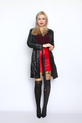 Full length portrait of blonde woman in leather black coat and red skirt holding umbrella in her hands. Over white background in studio