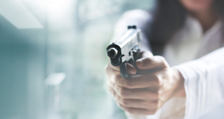 Woman pointing a gun at the target on blur background, criminal with gun, selective focus on front...