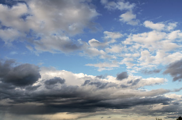 Obraz premium Cumulus clouds of fantastic shape soar in the sky in the sun's rays over the visible horizon line.