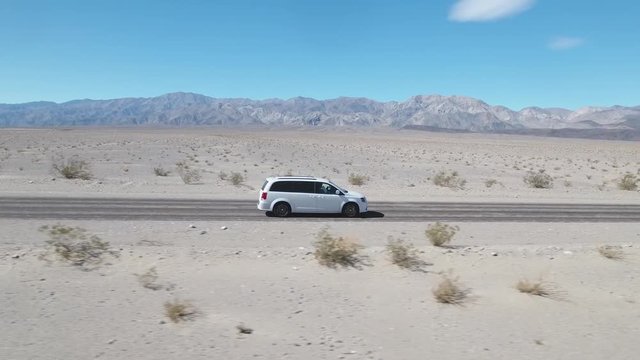 White minivan car driving along empty desert road at Death Valley, California