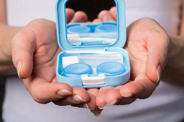 Beautiful hands hold soft contact lenses and a container for them.