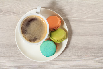 Cup of coffee and delicious macarons cakes of different color on white plate.