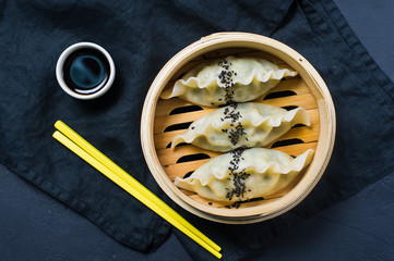 Japanese gyoza in a traditional steamer, yellow chopsticks. Dark background, side view