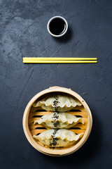 Japanese gyoza in a traditional steamer, yellow chopsticks. Dark background, top view