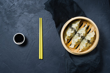 Korean dumplings in a traditional steamer, yellow chopsticks. Dark background, top view