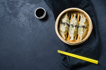 Japanese gyoza in a traditional steamer, yellow chopsticks. Dark background, top view, space for text