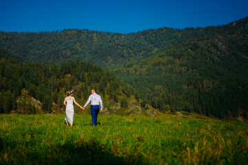 Fototapeta na wymiar Emotional wedding shot of the happy glamour newlywed couple walking on meadow in wild nature. Beautiful nature view.