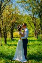 Stylish couple in love portrait, Newlywed husband and wife in circlet of flowers hugging near tree outdoors, summer nature concept, romantic couple on honeymoon resort